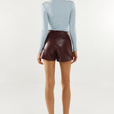 Person wearing a light blue long-sleeve top and brown leather shorts on a white background