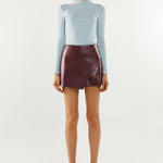 Person wearing a light blue long-sleeve top and maroon leather skirt on a white background