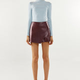 Person wearing a light blue long-sleeve top and maroon leather skirt on a white background