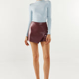 Person wearing a light blue sweater and maroon leather skirt on a white background